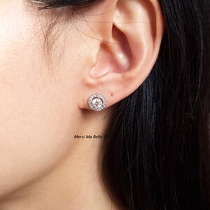 May include: A pair of silver stud earrings with a round, clear stone surrounded by smaller stones.