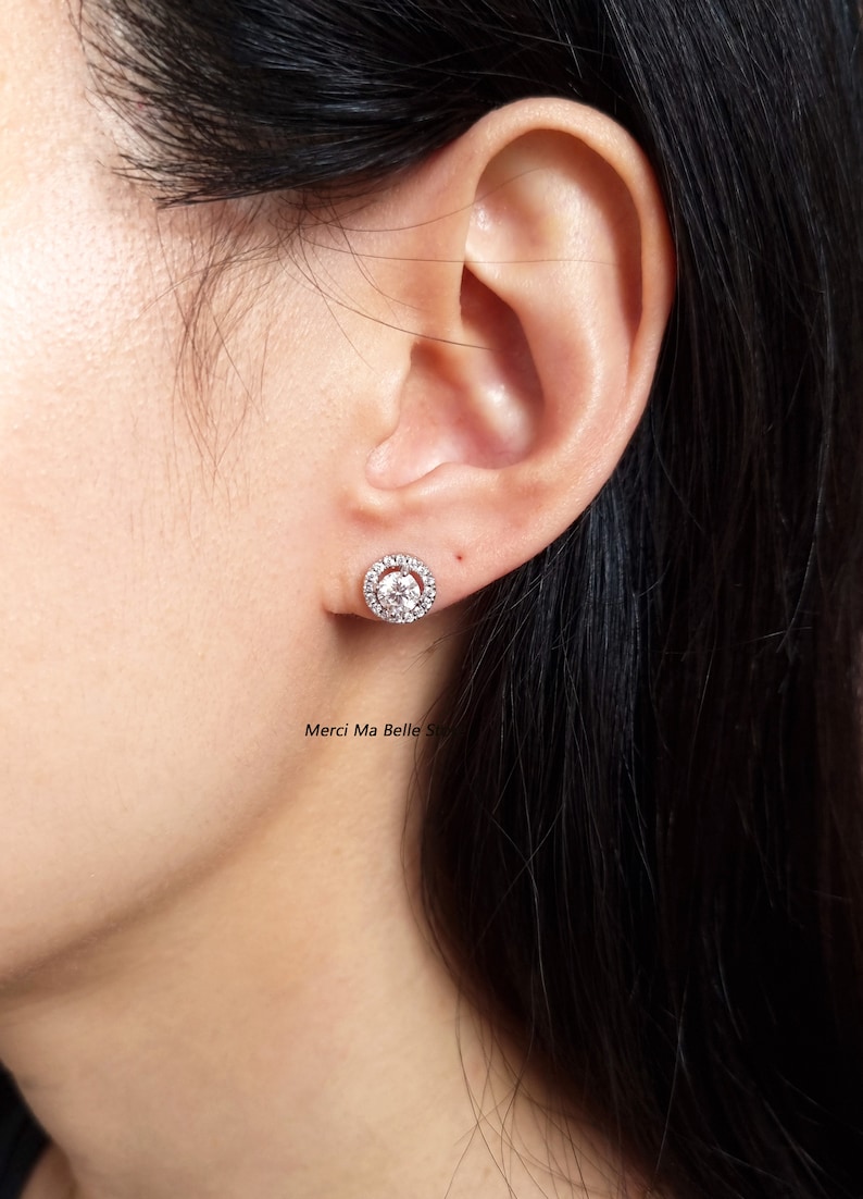 May include: A pair of silver stud earrings with a round, clear stone surrounded by smaller stones.