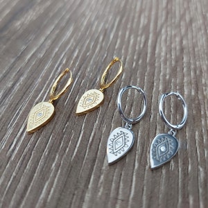 May include: Three pairs of earrings with a teardrop-shaped charm featuring an evil eye design. The charms are gold and silver and have a small clear stone in the center of the eye.