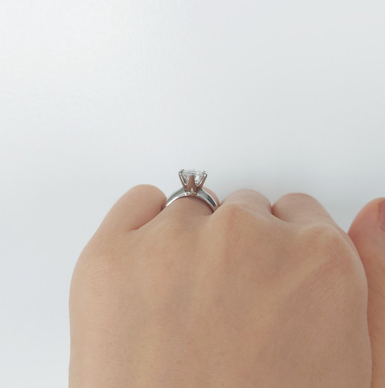 May include: A silver ring with a large, clear, round diamond set in a six-prong setting.
