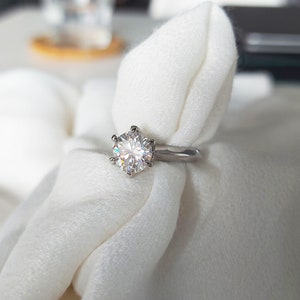 May include: A silver ring with a large, round, clear diamond set in a six-prong setting.