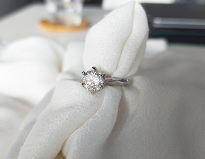 May include: A silver ring with a large, round, clear diamond set in a six-prong setting.