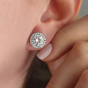 May include: A pair of silver stud earrings with a large round clear stone surrounded by a halo of smaller clear stones.