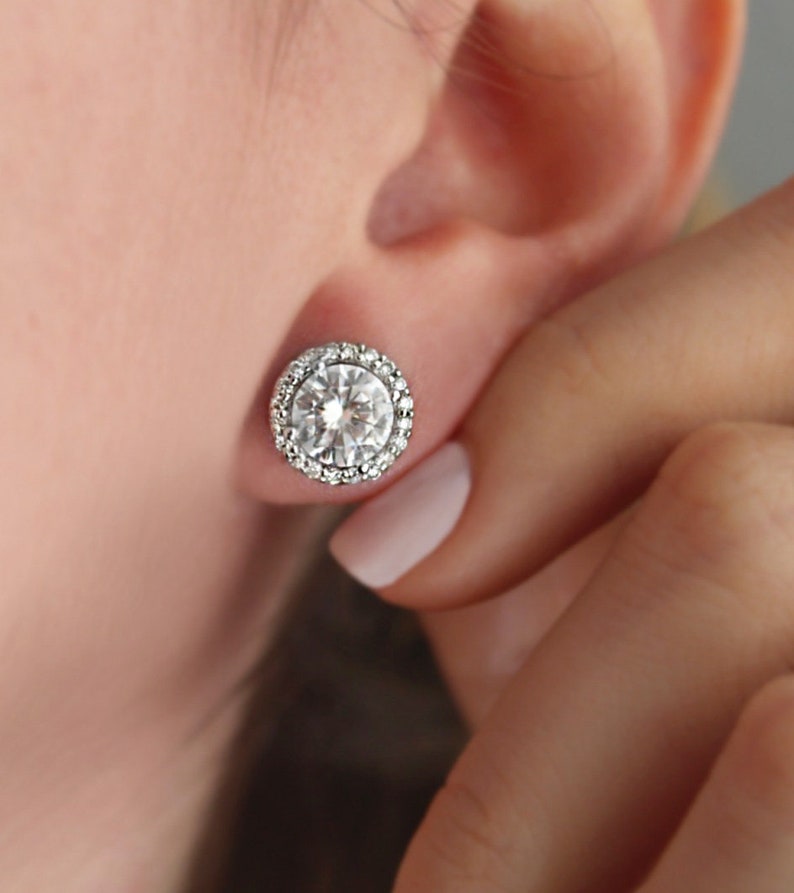 May include: A pair of silver stud earrings with a large round clear stone surrounded by a halo of smaller clear stones.