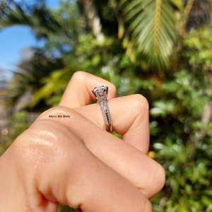 May include: A silver engagement ring with a large, round, clear diamond center stone. The band is set with smaller diamonds and has a delicate, intricate design.