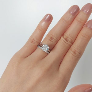 May include: A close-up of a hand wearing a silver engagement ring with a large, round diamond and a matching silver wedding band with smaller diamonds.
