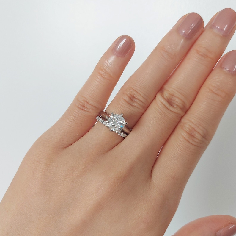 May include: A close-up of a hand wearing a silver engagement ring with a large, round diamond and a matching silver wedding band with smaller diamonds.