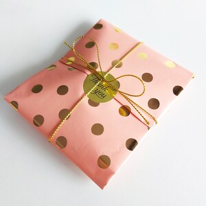 May include: A pink gift bag with gold polka dots and a gold ribbon. A gold sticker with the text "Thank you" is attached to the ribbon.