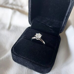 May include: A silver engagement ring with a large, clear diamond in a black velvet ring box.