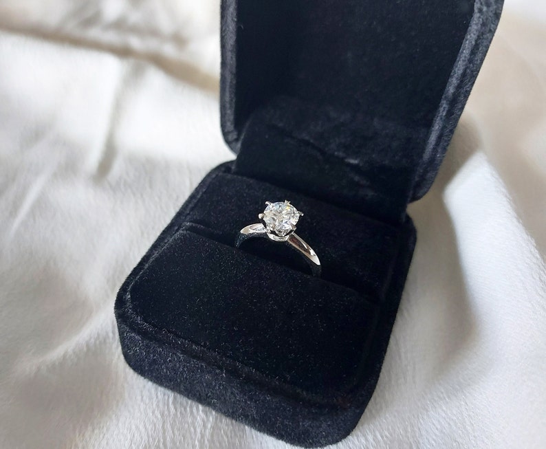 May include: A silver engagement ring with a large, clear diamond in a black velvet ring box.