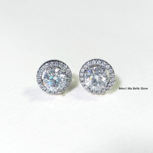 May include: A pair of silver stud earrings with a round, clear stone surrounded by a halo of smaller stones.