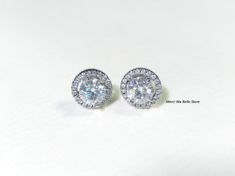 May include: A pair of silver stud earrings with a round, clear stone surrounded by a halo of smaller stones.