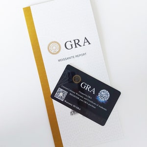 May include: A white and gold certificate with the text "GRA Moissanite Report" and a black card with the text "GRA Created by GRA Limited Lifetime Warranty and Certificate of Authentic REGISTER your GRA purchase Warranty ID:GRA".