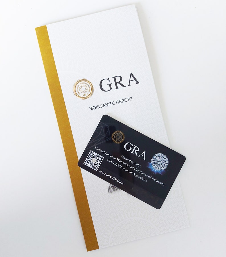 May include: A white and gold certificate with the text "GRA Moissanite Report" and a black card with the text "GRA Created by GRA Limited Lifetime Warranty and Certificate of Authentic REGISTER your GRA purchase Warranty ID:GRA".