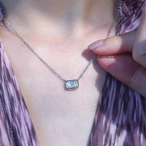 May include: A silver chain necklace with a clear emerald-cut gemstone pendant.