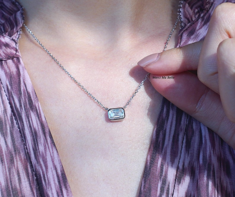 May include: A silver chain necklace with a clear emerald-cut gemstone pendant.