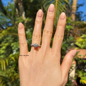 May include: A close-up of a hand wearing a silver ring with a large, round, clear diamond. The ring has a delicate, intricate design. The text "Merci Ma Belle" is visible in the image.