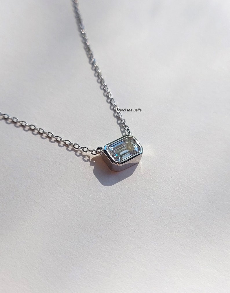 May include: A silver chain necklace with a single, clear, emerald-cut gemstone pendant.