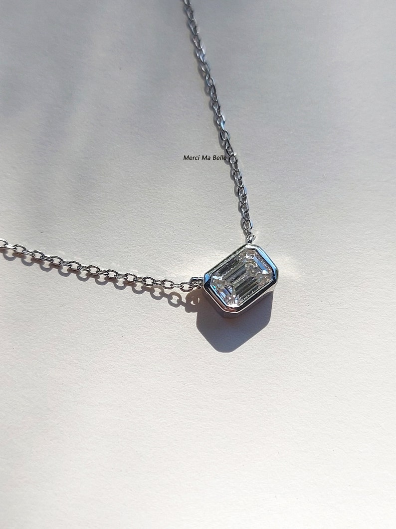 May include: A silver chain necklace with a rectangular pendant featuring a large, clear emerald-cut gemstone.