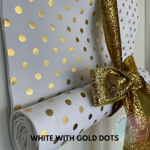 Puede incluir: Tela blanca con lunares dorados enrollada y atada con una cinta dorada. La tela está etiquetada con "WHITE WITH GOLD DOTS" y "CUTE CREATIONS BY CHLOE".