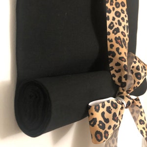 May include: A black fabric roll with a leopard print ribbon tied around it. The ribbon is tied in a bow.