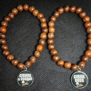May include: Two brown wooden bead bracelets with silver charms. One charm says "CIGARS & COGNAC" and the other says "CIGAR BOSS".