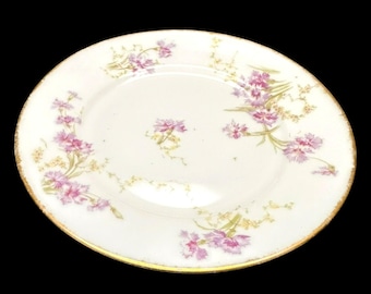 Peut inclure: Une assiette en céramique blanche avec un bord doré et un motif floral. L'assiette présente des fleurs roses et violettes avec des tiges vertes et des accents jaunes. L'assiette est ronde et a un aspect légèrement usé.