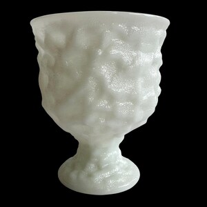 Op de afbeelding: Een witte, getextureerde glazen beker met een voet. De beker heeft een ruw, ongelijkmatig oppervlak, waardoor hij een unieke, organische uitstraling heeft. De steel en voet zijn ook getextureerd en het algehele ontwerp is eenvoudig maar elegant.