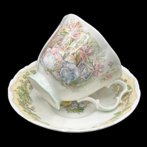 Puede incluir: Juego de taza y platillo de té blanco con una ilustración caprichosa de ratones en un jardín. La taza y el platillo tienen un borde festoneado con un borde floral amarillo. El asa de la taza es curvada.