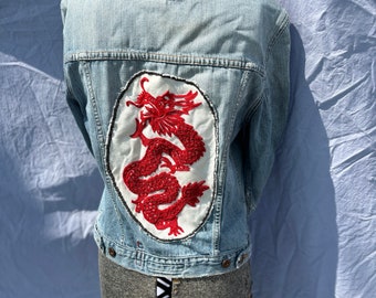 May include: A light blue denim jacket with a red embroidered dragon patch on the back.