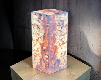 May include: A square, translucent, light fixture made of onyx with a brown and white marbled pattern. The fixture is illuminated from within, casting a warm glow.