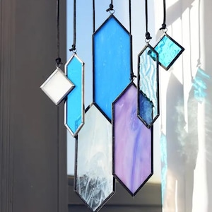 May include: A set of six stained glass window hangings in various shapes and colors, including blue, purple, and white. The hangings are suspended from black cords.