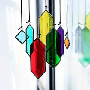 May include: A set of seven stained glass suncatchers hanging from black cords. The suncatchers are in various shapes and colors, including red, green, yellow, blue, purple, and orange.