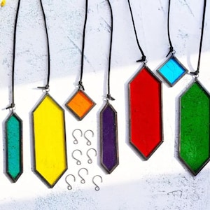 May include: A set of seven stained glass suncatchers, each with a different color and shape. The suncatchers are suspended from black cords and have metal hooks. The colors include green, yellow, orange, red, purple, and blue.