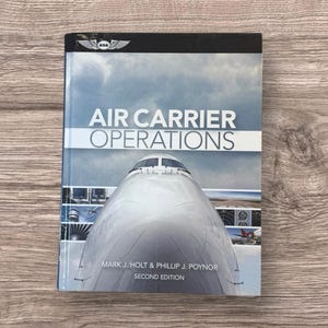 May include: A textbook titled "Air Carrier Operations" with a photo of an airplane on the cover. The book is a second edition by Mark J. Holt & Phillip J. Poynor. The cover has a blue and white color scheme.