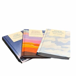 May include: Three hardcover books with nature-themed titles: "Star Gazing", "Sunset Seeking", and "Cloud Spotting". The books have colorful covers depicting a starry night, a sunset, and a cloudy sky. The titles are in a serif font.