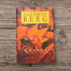 May include: A hardcover book titled "Never Change" by Elizabeth Berg. The cover features a background of orange and red autumn leaves. The author's name is in a gold rectangle at the top. The title is in white script.