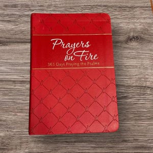 May include: A red book with the title "Prayers on Fire" in white script. The book cover has a diamond pattern with flame-shaped designs. The text "365 Days Praying the Psalms" is also visible on the cover.