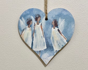 May include: A wooden heart-shaped ornament with a blue background and three painted angels in white dresses. The angels have brown hair and wings.