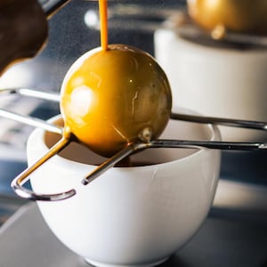 Coffee Alive stainless steel blanching tool across an espresso cup under portafilter, showing chilling ball in use