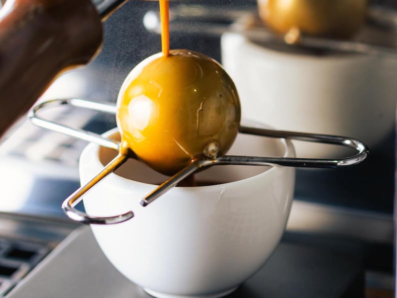 Coffee Alive stainless steel blanching tool across an espresso cup under portafilter, showing chilling ball in use
