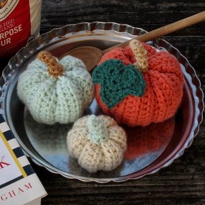 May include: Three crocheted pumpkins on a silver tray. One pumpkin is light blue, one is orange, and one is cream colored.