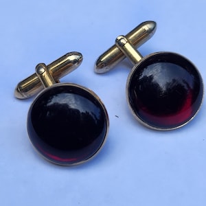 May include: A pair of gold cufflinks with round, dark red glass stones.