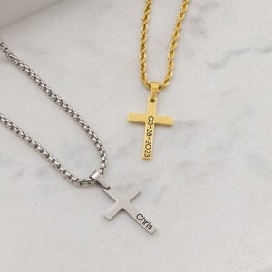 May include: Two silver and gold necklaces with cross pendants. The gold cross has the date "03-28-2023" engraved on it. The silver cross has the name "Chris" engraved on it.