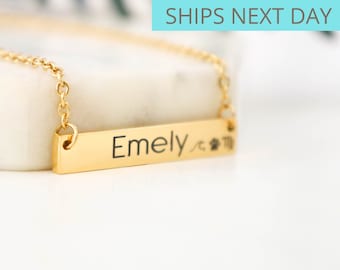 May include: Gold bar necklace with the name "Emely" and a zodiac symbol engraved on it.
