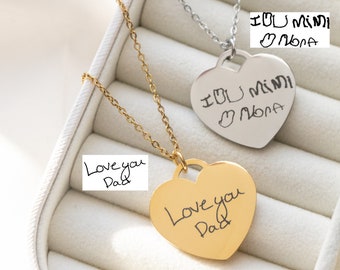 May include: Two heart-shaped pendant necklaces. One is gold-toned with the inscription "Love you Dad". The other is silver-toned with the inscription "I ❤️ Mimi Nora". Both pendants hang from delicate chains, displayed in a jewelry box.