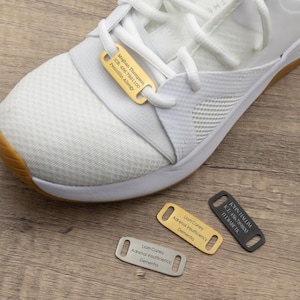 Puede incluir: Tres etiquetas de zapatos de oro y plata con texto grabado. Las etiquetas son para información médica e incluyen nombres, condiciones médicas y números ICE. Las etiquetas están sobre una superficie de madera.