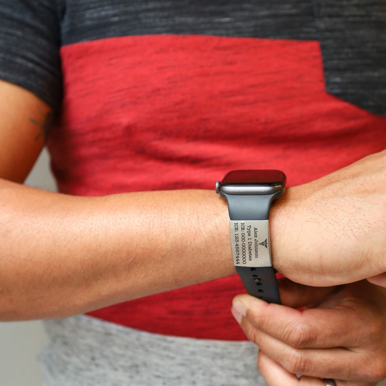 K&ouml;nnte beinhalten: Eine schwarze Apple Watch mit einem schwarzen Armband. Das Armband hat ein silbernes medizinisches Warnh&auml;ufchen mit der Gravur "Alex Johnson", "Typ-1-Diabetes", "123-000-0000" und "108-123-4567".