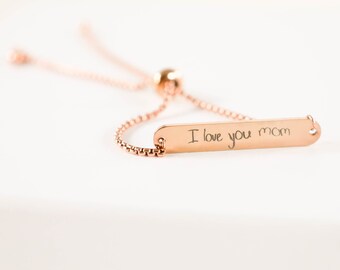 May include: A rose gold adjustable bracelet with a rectangular charm that says "I love you mom" in cursive handwriting.