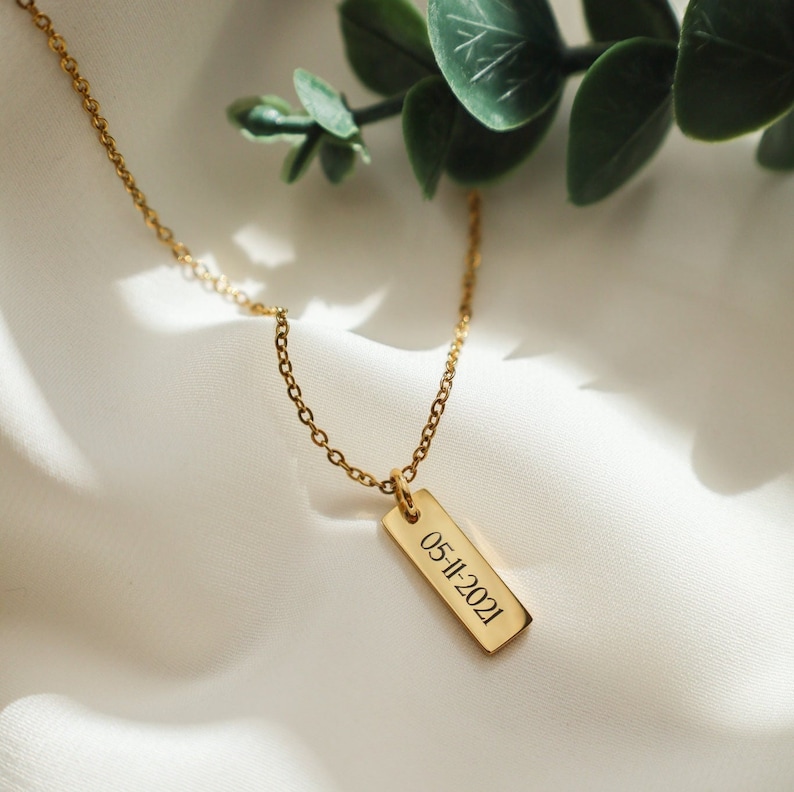 May include: A gold chain necklace with a rectangular pendant engraved with the date "05-11-2021".